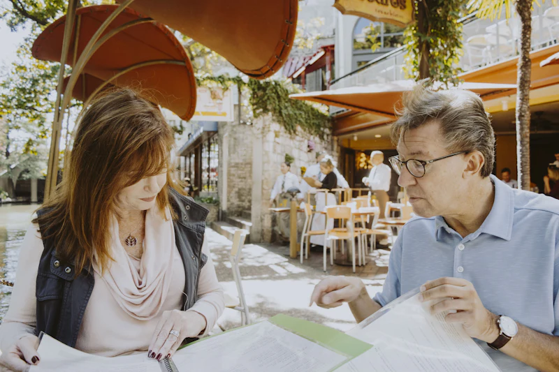 Two people reading through papers together at an outdoor cafe table